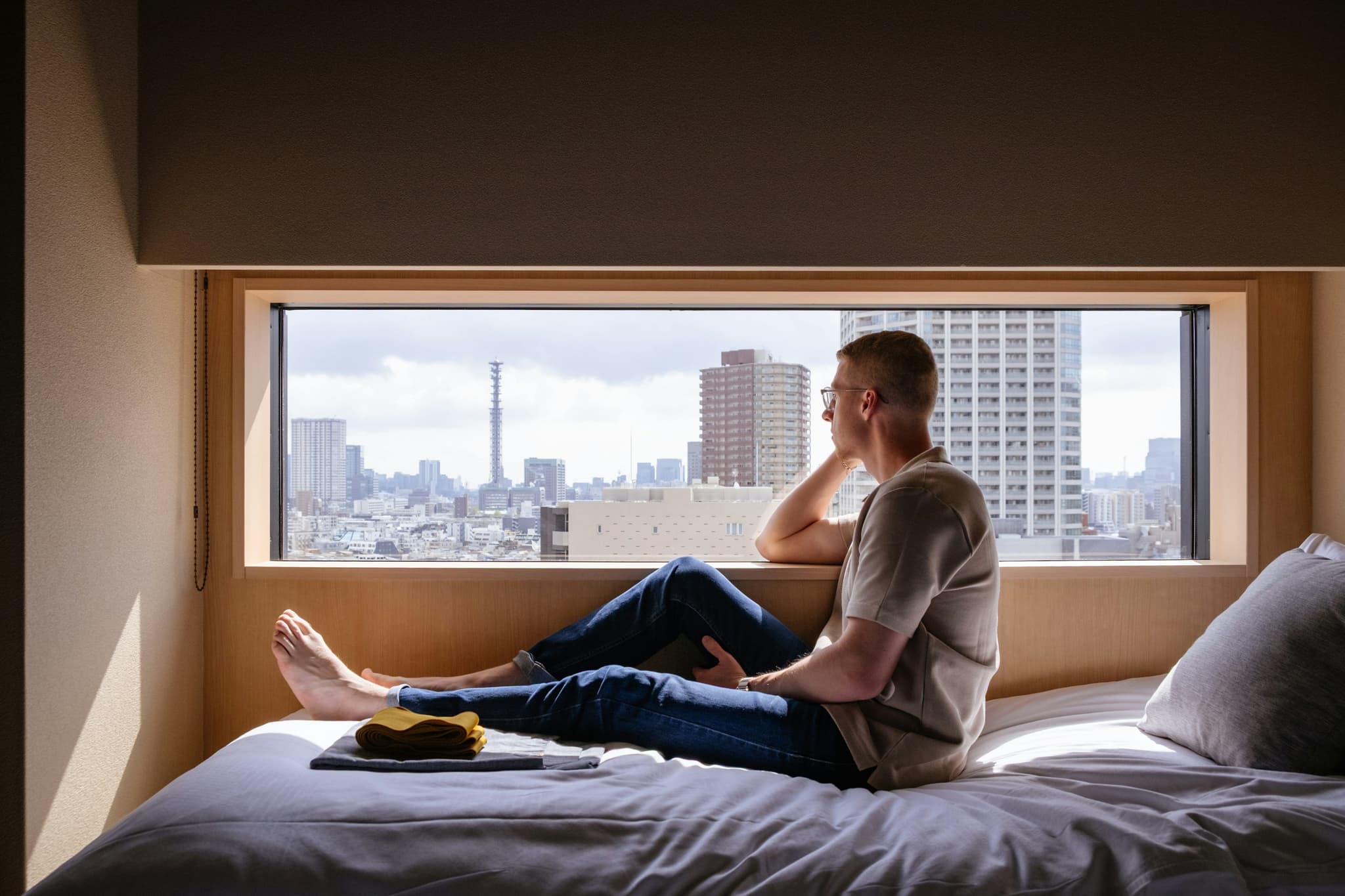  Man relaxes on a bed, gazing at a city view.